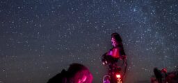 Sternenhimmel über einer Person bei der Arbeit an einem Teleskop mit Rotlicht