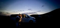 Dämmerung, ein Auto mit offener Tür, dahinter ein Hügelkamm