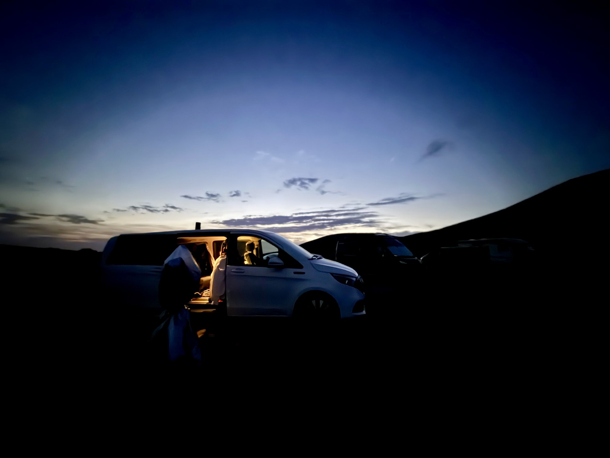 Dämmerung, ein Auto mit offener Tür, dahinter ein Hügelkamm